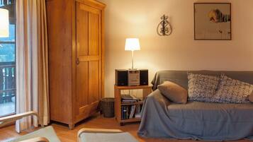 Une pièce chaleureuse avec une armoire en bois, un téléviseur posé sur une petite table, un canapé agrémenté de coussins à motifs et une fenêtre avec des rideaux.