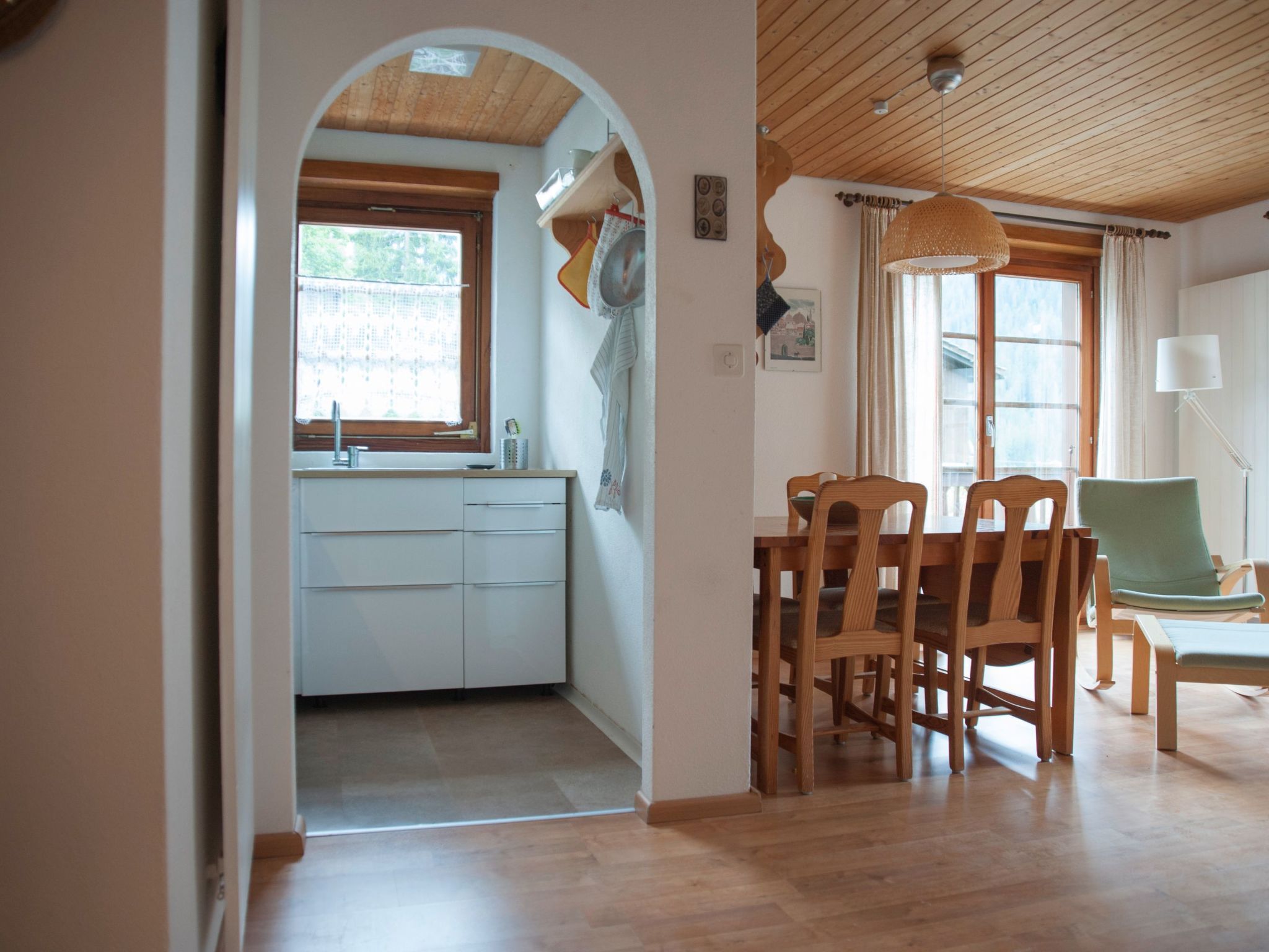 Une cuisine avec une fenêtre, des placards en bois et un coin repas comprenant des chaises et une table.