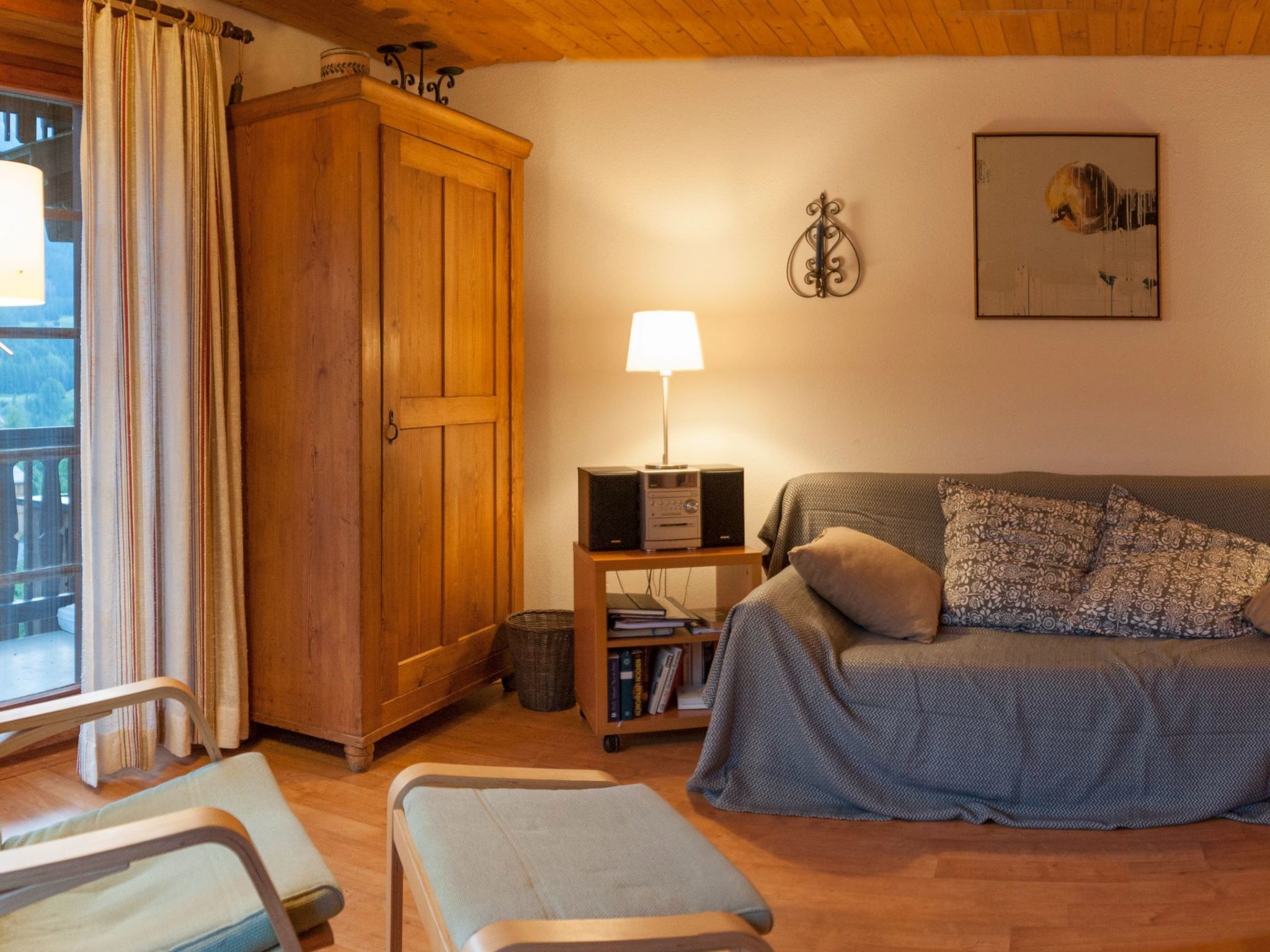 Un salon chaleureux avec une armoire en bois, un canapé agrémenté de coussins à motifs, une petite table avec une lampe et une bibliothèque.