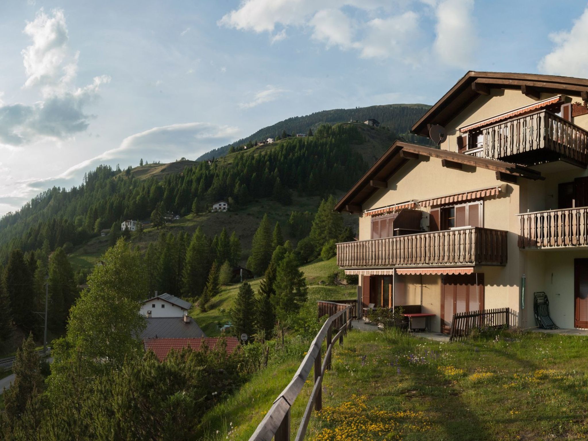 Un immeuble à deux étages doté de balcons, entouré d’une colline boisée.