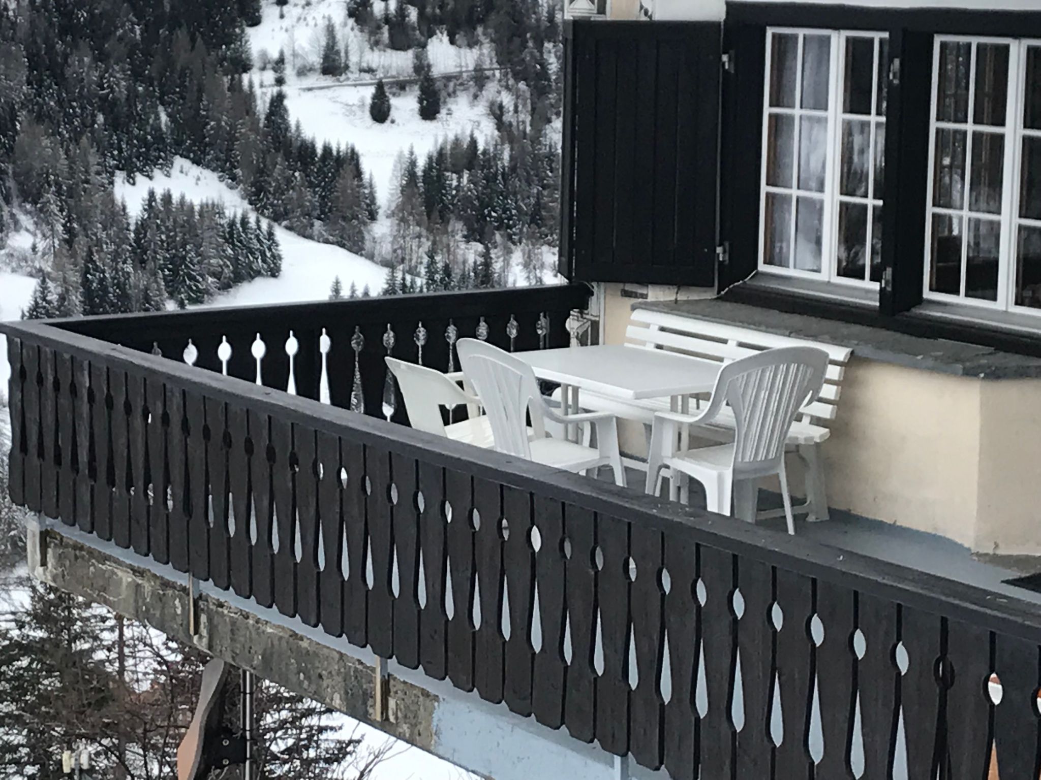 A balcony with a table and chairs, overlooking a snowy mountain landscape.