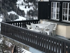 Un balcon avec une table et des chaises, donnant sur un paysage montagneux enneigé.