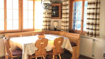 Un coin repas avec une table et des chaises en bois, un luminaire suspendu et des rideaux à motifs.