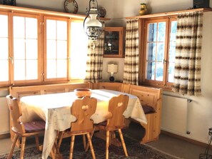 Un coin repas avec une table et des chaises en bois, un luminaire suspendu et des rideaux à motifs.
