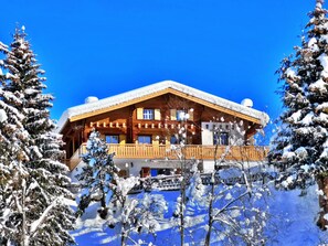Eine Holzhütte mit einem Balkon, umgeben von schneebedeckten Bäumen.