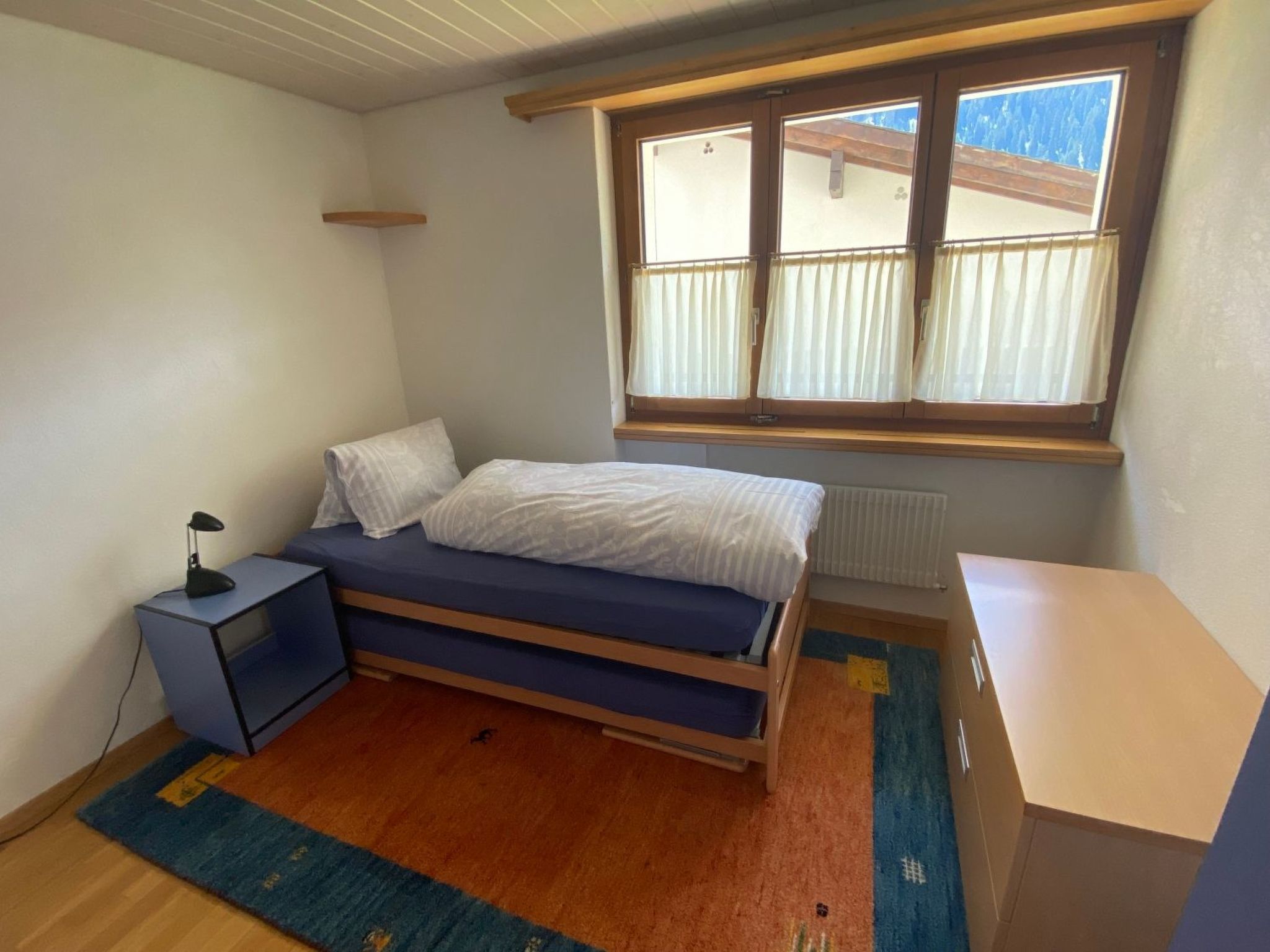 Una camera da letto con un letto, una scrivania, una sedia, una finestra con tende e un termosifone.