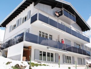 Un immeuble à plusieurs étages doté de balcons, de grandes fenêtres et, en arrière-plan, d’une piste de ski.