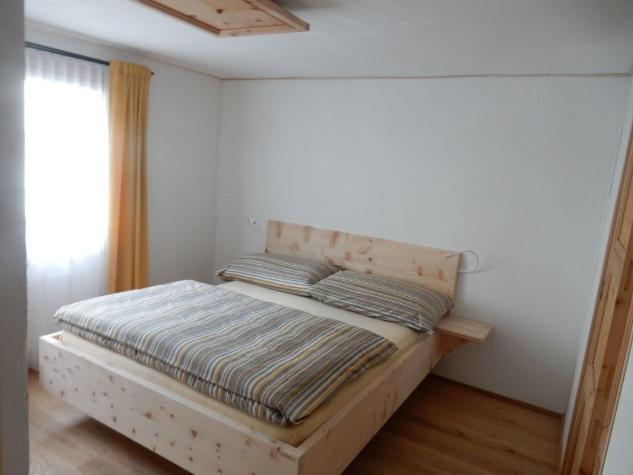Un lit simple avec une tête de lit en bois et une couvre-lit à rayures, dans une pièce aux murs blancs et au plancher en bois.