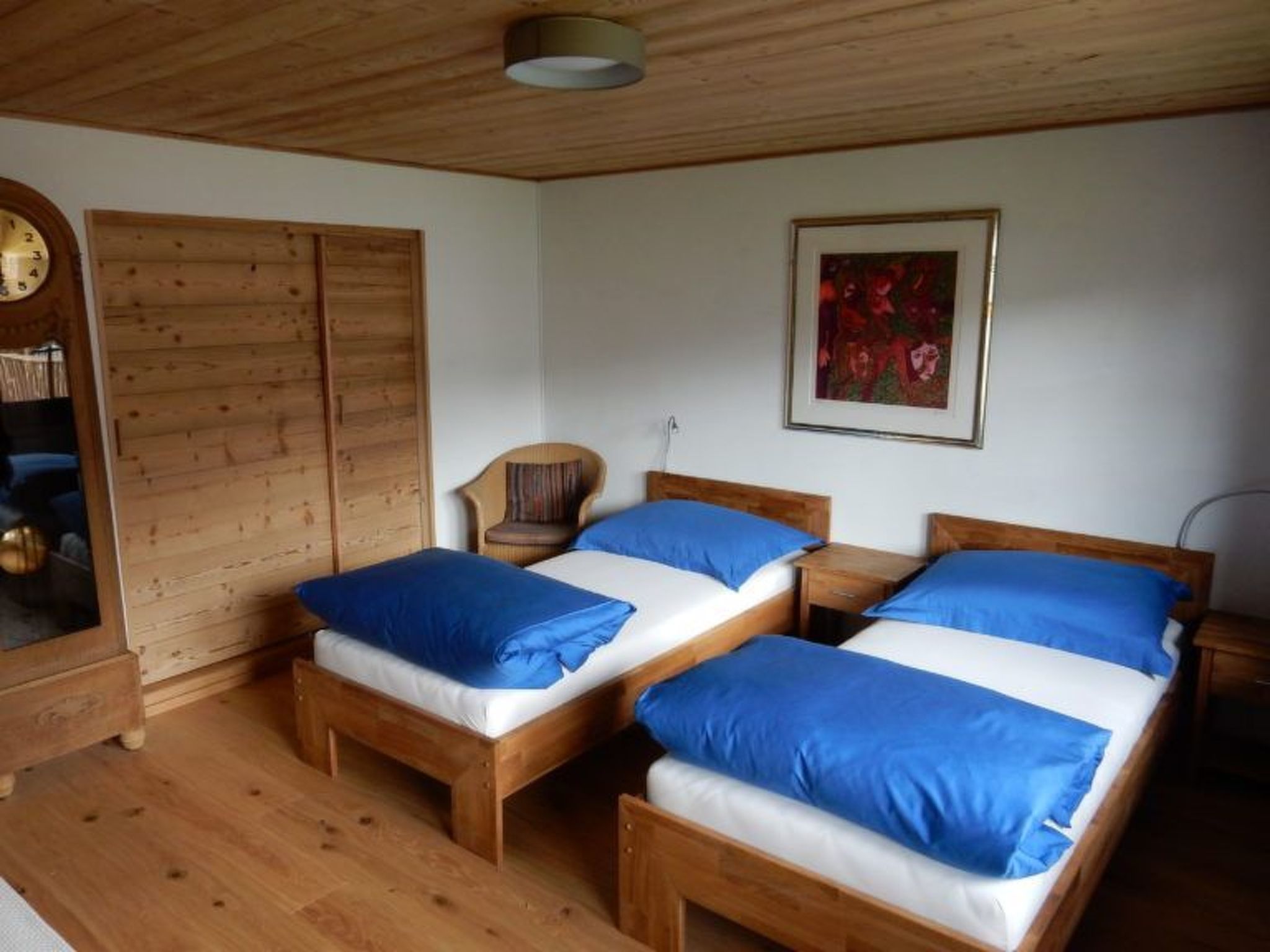 A room with two wooden beds, a wooden wardrobe, a chair, and a painting on the wall.