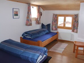 Ein Zimmer mit zwei Holzbett, einem Holzstuhl, einem Fenster mit Vorhängen und einer Heizung.