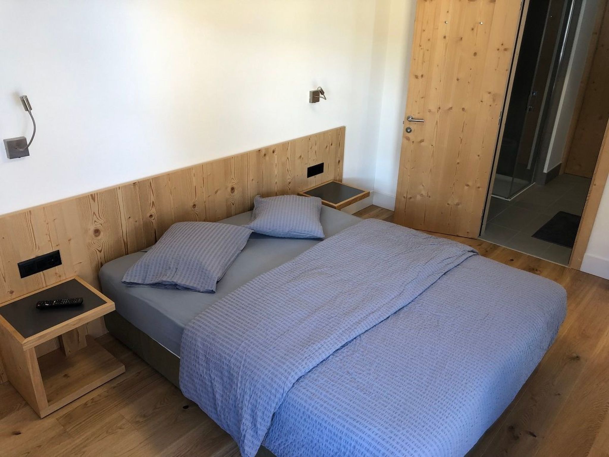 A bedroom with a wooden headboard, a bed with a blue blanket, two bedside tables, and a nightstand with a remote control.