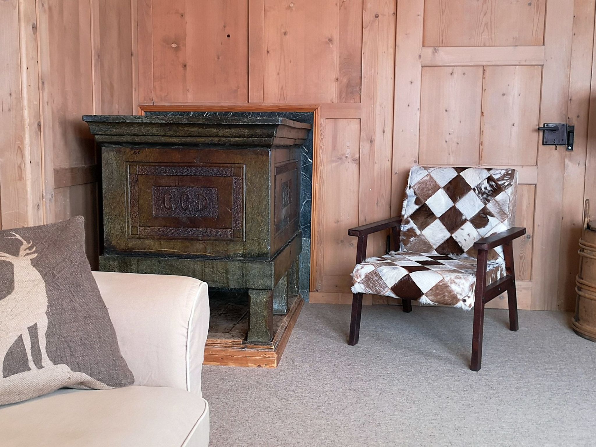 Une pièce avec un mur en bois, une cheminée en pierre, un fauteuil à motifs et un canapé blanc avec un coussin.