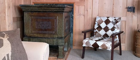 Quarto com parede de madeira, lareira de pedra, poltrona estampada e sofá branco com almofada.