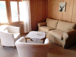 Una habitación con un sofá color beige, un sillón blanco y una pequeña mesa con mantel a cuadros.
