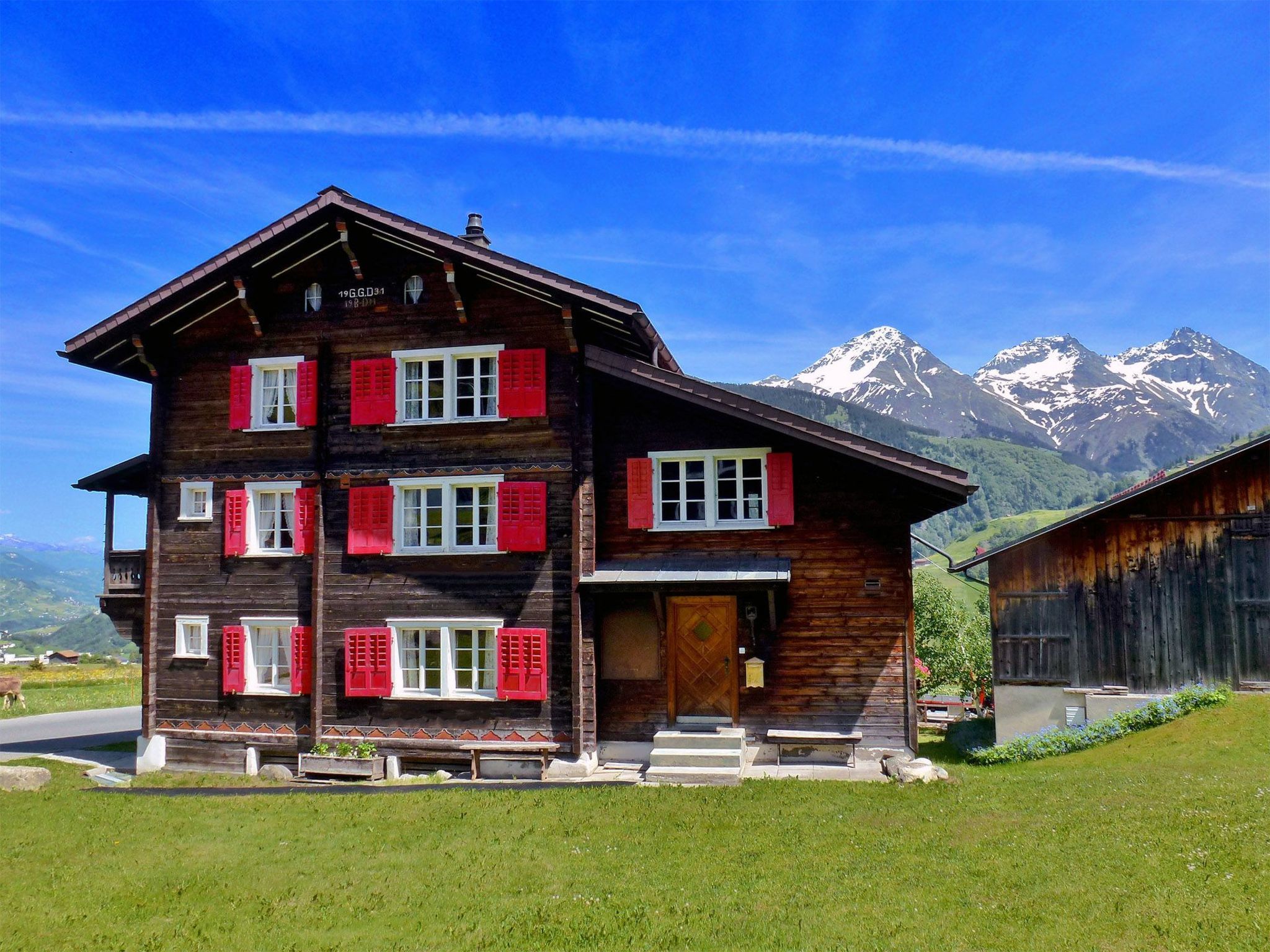 Ein mehrstöckiges Holzhaus mit roten Fensterläden, einer Veranda und einem Berg im Hintergrund.