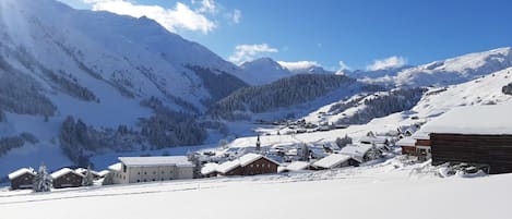 A snow-covered village with traditional wooden houses and a church, surrounded by mountains.