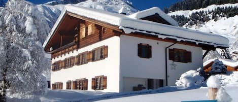 A snow-covered lodge with a wooden exterior and a balcony, surrounded by mountains.