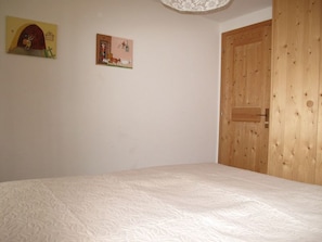 A bedroom with a wooden door, a bed with a white textured mattress, and two wall-mounted pictures. - Casa Posta Berther-Roth, (Rueras/Sedrun), 663.01 by Interhome (Rueras Dieni)