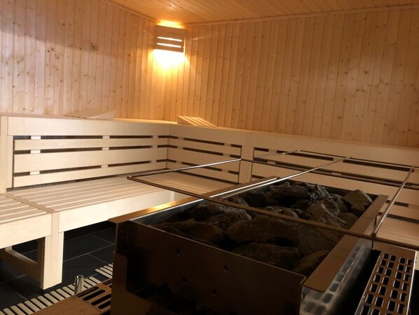 A sauna with wooden benches, a heated stone floor, and a sloped ceiling.
