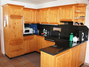 A kitchen with wooden cabinets, a microwave, a coffee maker, and a kettle on the countertop. - Casa Mulinera 2 Derycke, (Camischolas/Sedrun), 243.02 by Interhome (Camischolas)