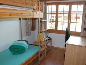 A dormitory room with bunk beds, a desk, and a window with a view of buildings. - Casa Mulinera 2 Derycke, (Camischolas/Sedrun), 243.02 by Interhome (Camischolas)