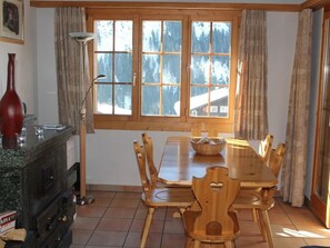 A dining area with a wooden table and chairs, a window with a view of trees, and a red vase on the counter. - Casa Mulinera 2 Derycke, (Camischolas/Sedrun), 243.02 by Interhome (Camischolas)