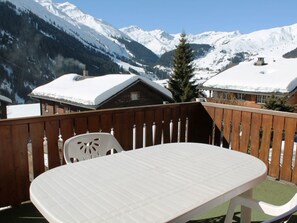 A wooden deck with a white table and chairs, overlooking snow-covered mountains. - Casa Mulinera 2 Derycke, (Camischolas/Sedrun), 243.02 by Interhome (Camischolas)