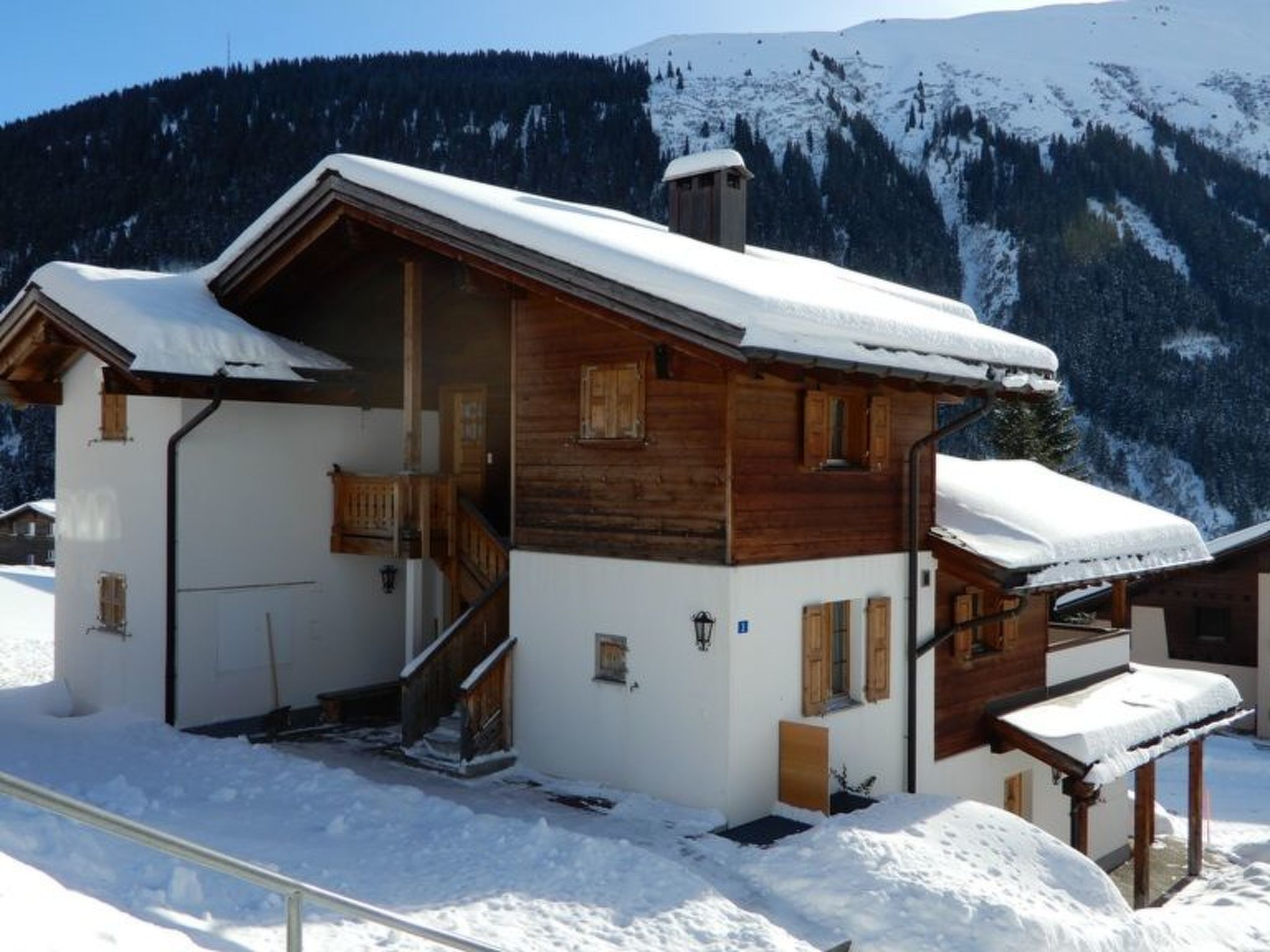 Un chalet en bois doté d’un balcon, d’un escalier et d’un toit recouvert de neige.