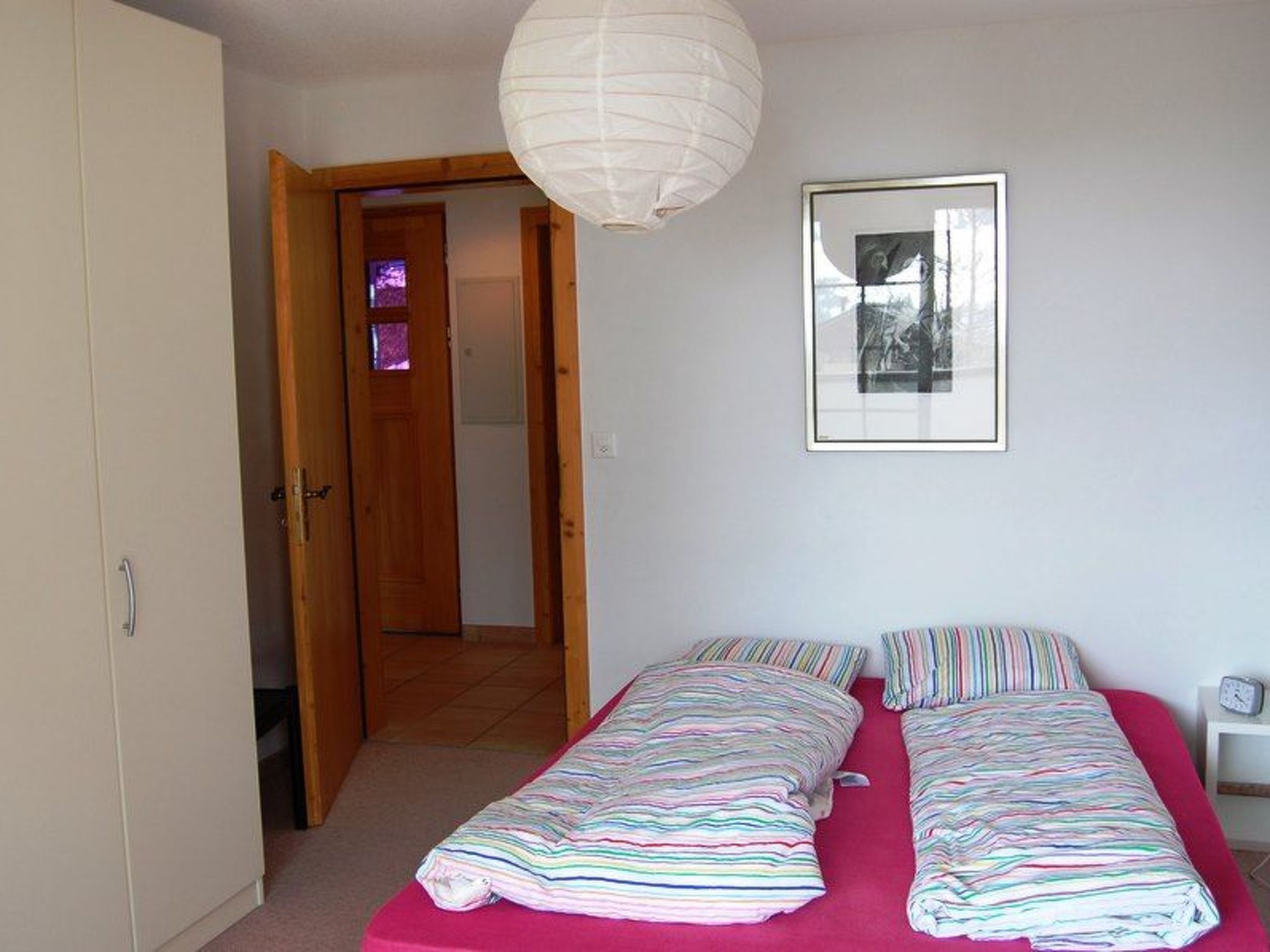 A bedroom with a bed, a door, a window, and a wall-mounted picture.