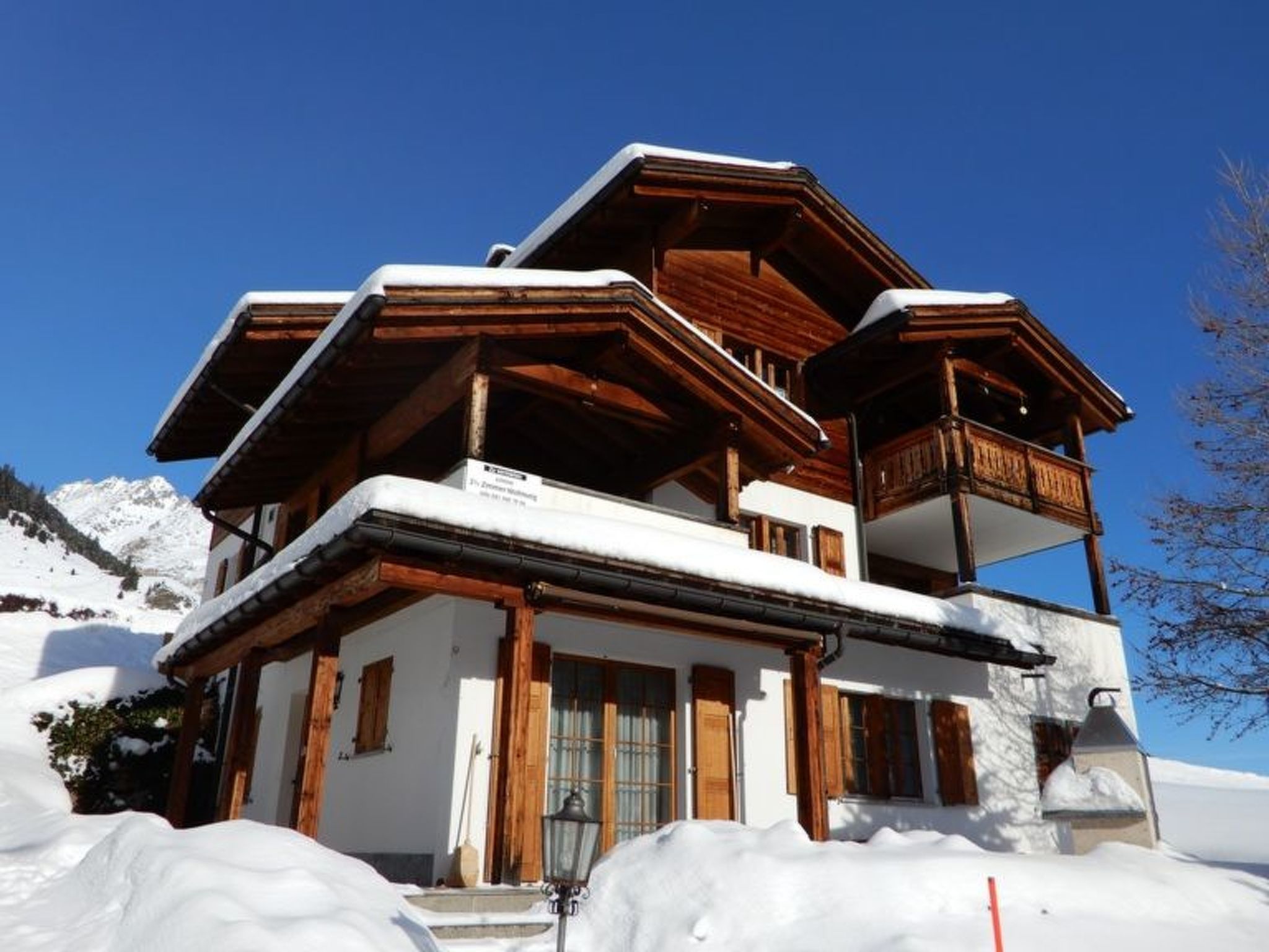 A multi-story wooden chalet with a balcony, surrounded by snow.