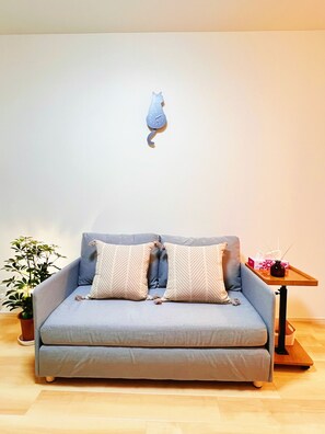 A grey sofa with patterned cushions, a small table with a vase and tissues, and a wall-mounted cat decoration. - 4min walk JR Kyobashi · Entire home · 7guests · Renovated · Walk to Osaka Castle (大阪市)