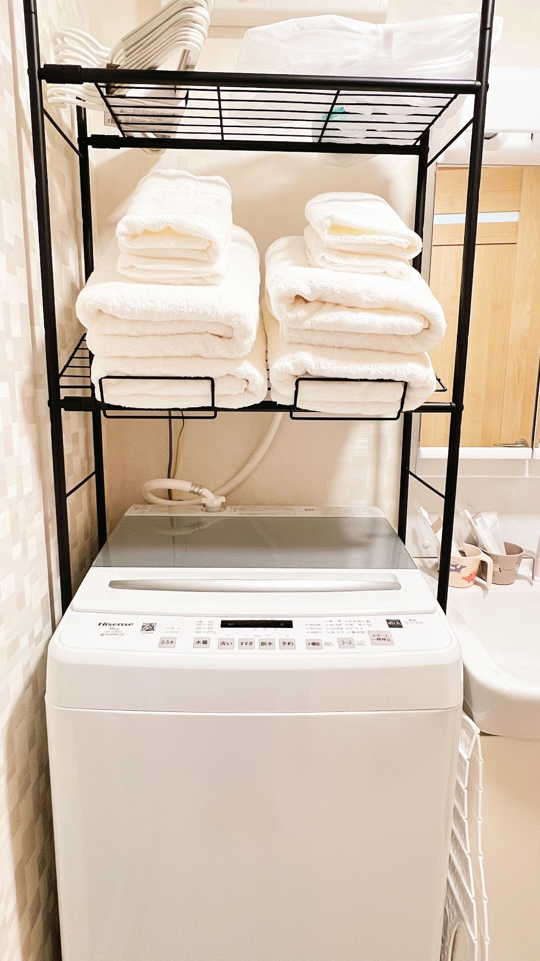A laundry area with a stacked washer and dryer, a metal shelf with folded towels, and a white tiled wall.