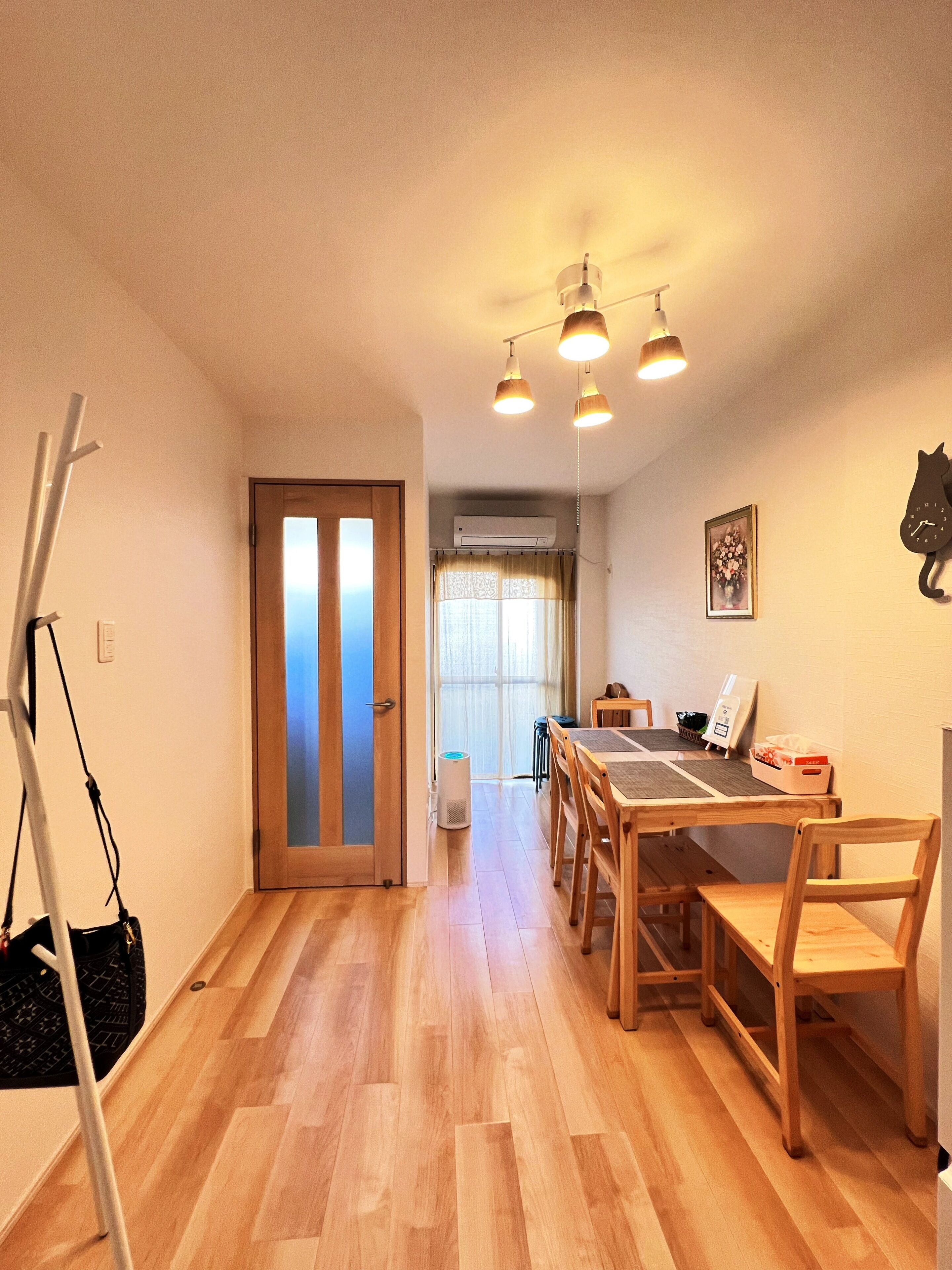 A room with a wooden floor, a dining table with chairs, a coat rack, and a door leading to another room.