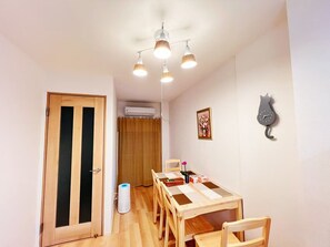 A dining area with a wooden table and chairs, an air conditioning unit, a cat-shaped clock, and a door with vertical blinds. - 4min walk JR Kyobashi · Entire home · 7guests · Renovated · Walk to Osaka Castle (大阪市)