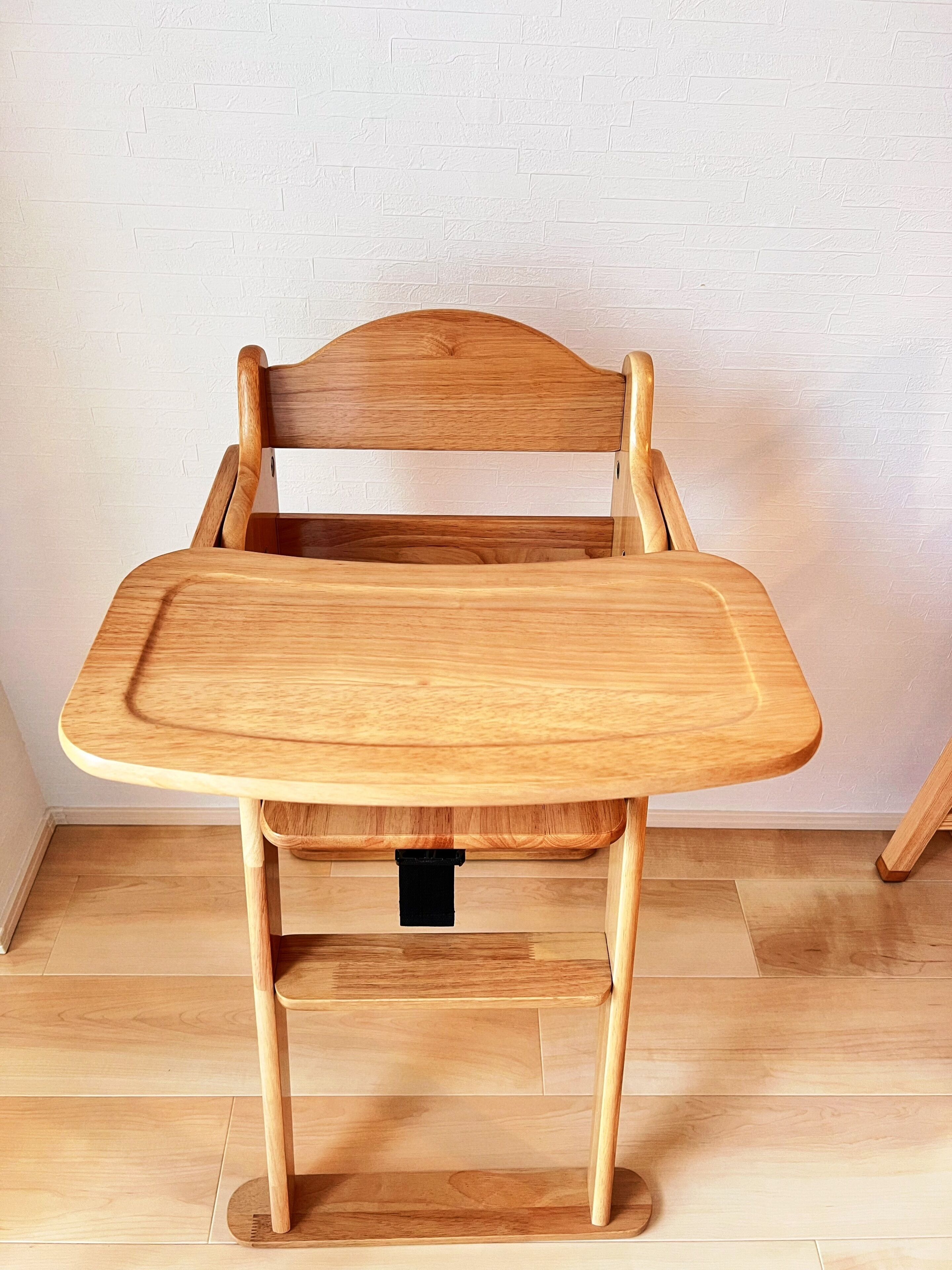 A wooden chair with a tray table against a white brick wall.
