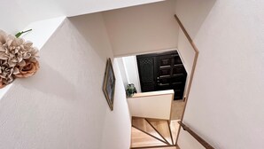 Eine Treppe führt zu einem Raum mit einer dunklen Holztür, einem gerahmten Bild an der Wand und einem Blumentopf.