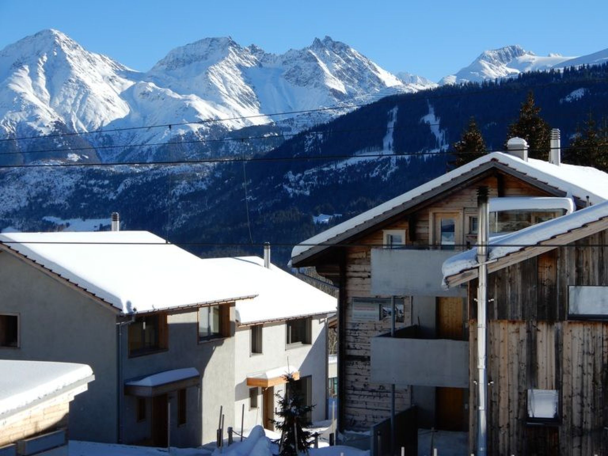 Un chalet de montagne avec une façade en bois, un balcon et une vue sur les sommets enneigés.