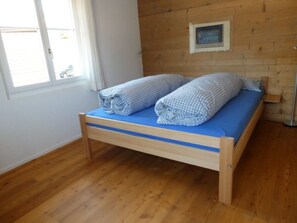 A single bed with a blue mattress and two rolled-up pillows in a room with wooden walls and a window. - Huber, (Sedrun), 156.01 by Interhome (Sedrun)