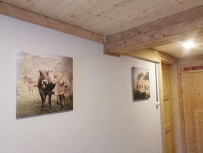 Un couloir avec des poutres en bois au plafond, des murs blancs et deux tableaux représentant des vaches.