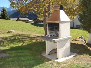 A stone barbecue grill with a chimney, set on a grassy lawn with a mountain backdrop. - Londadusa Parterre, (Rueras/Sedrun), 178.02 by Interhome (Rueras Dieni)
