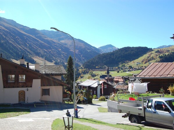 Un pueblo rural con casas tradicionales, un farol y montañas al fondo.