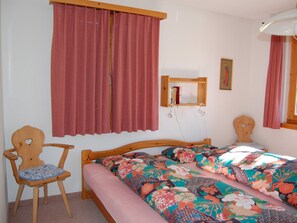 Un dormitorio con una cama de madera, una silla, un espejo y una ventana con cortinas.