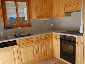 A kitchen with wooden cabinets, a dishwasher, an oven, and a window with lace curtains. - Londadusa Parterre, (Rueras/Sedrun), 178.02 by Interhome (Rueras Dieni)