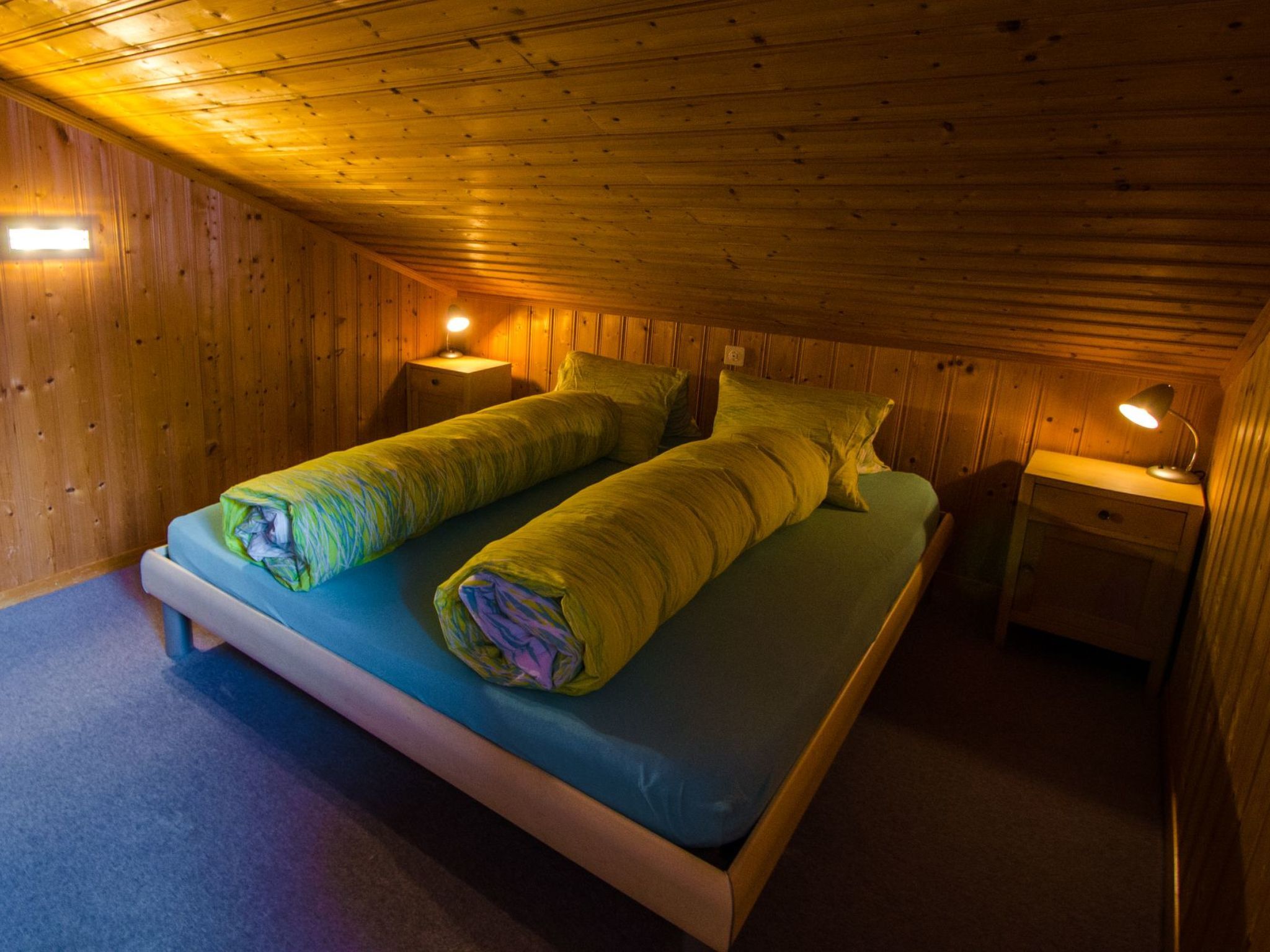 Una habitación con paneles de madera, una cama, dos mesitas de noche y un ventanal.