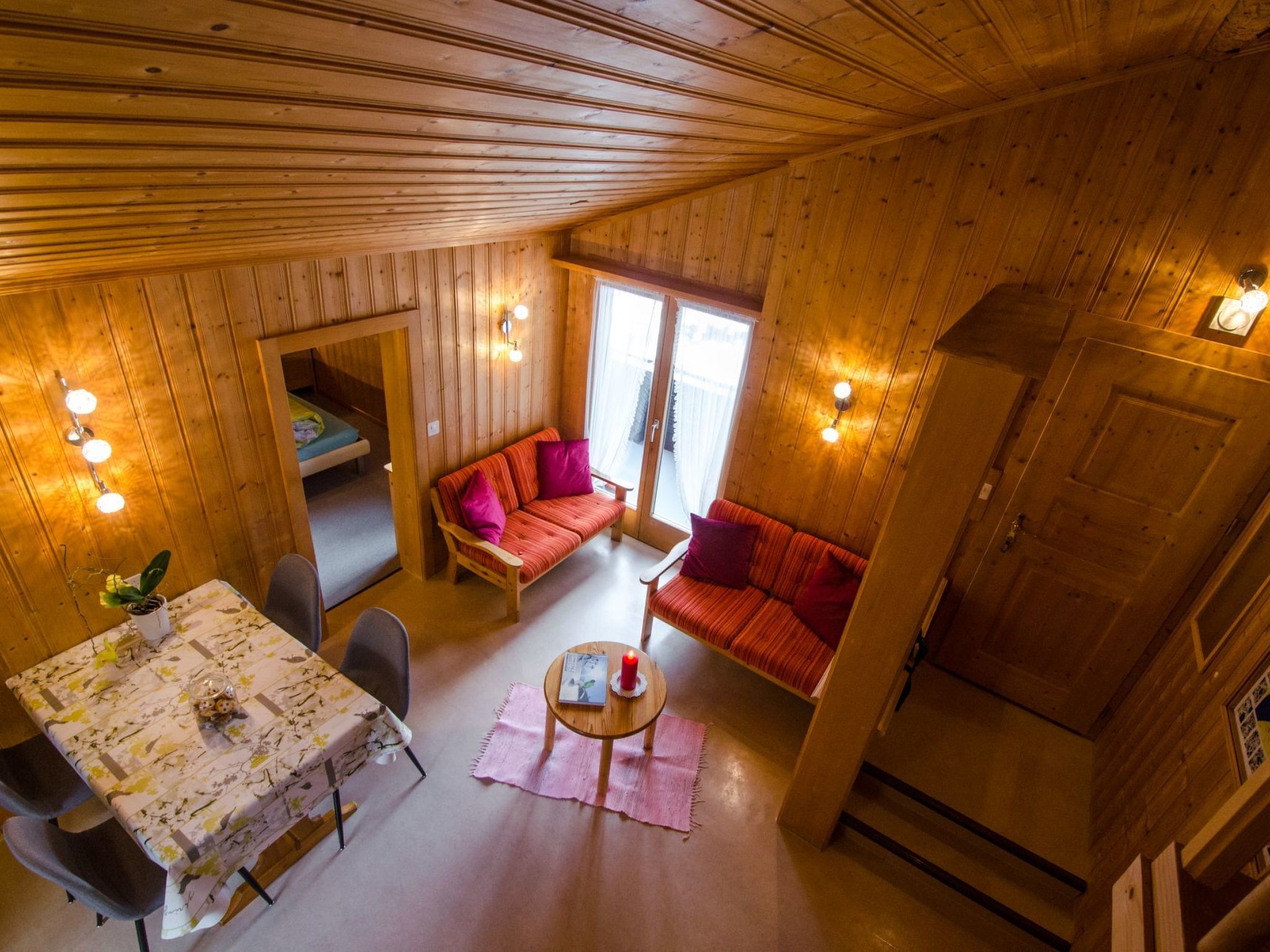 A wooden cabin interior with a dining area, a sofa, and a bed.