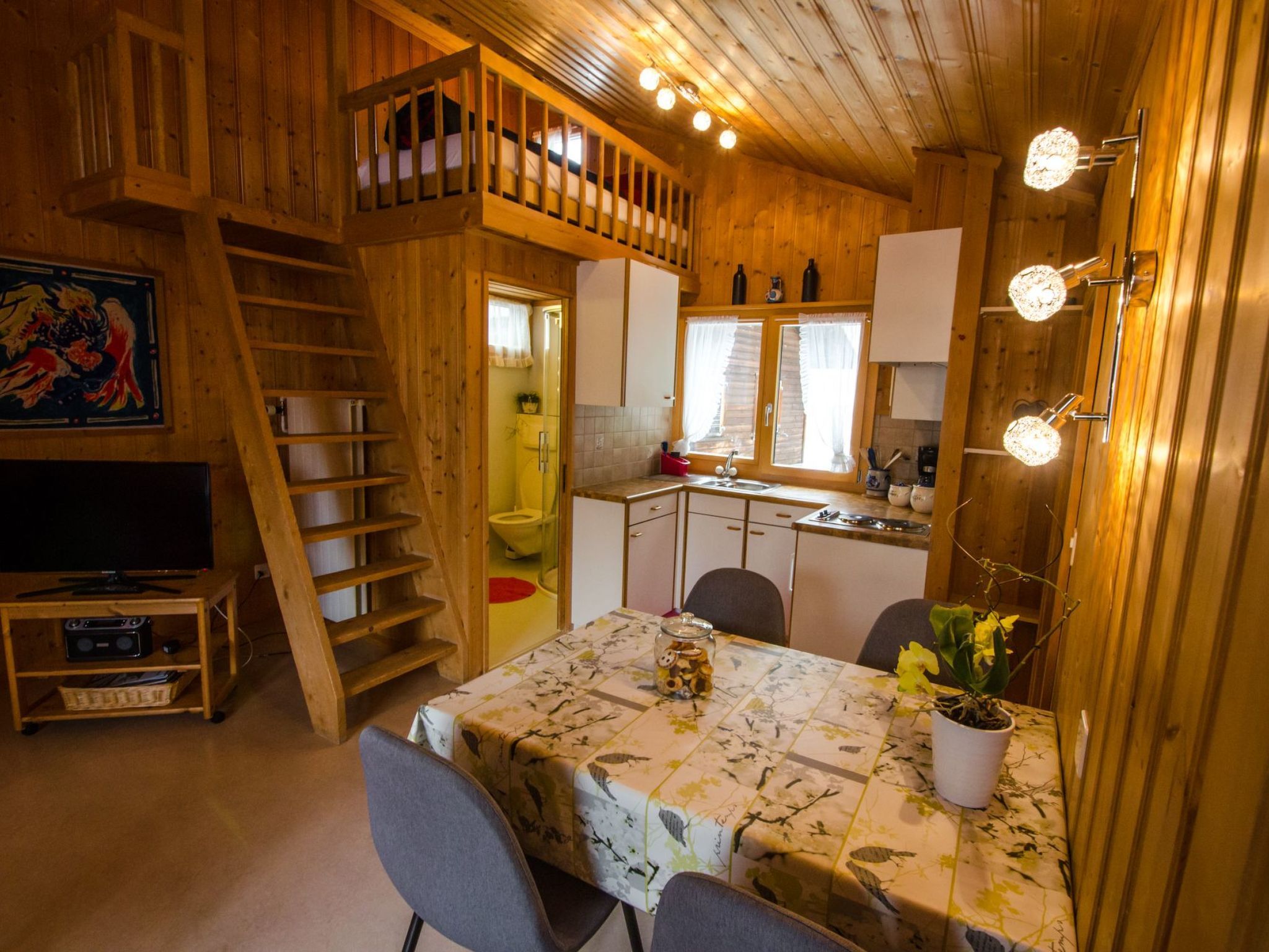A cozy cabin interior with a dining area, kitchen, and a loft bedroom.