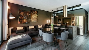 A modern living room with a sofa, a dining table, and chairs. There is a kitchen area with a refrigerator and a coffee machine. - Villa Violetta (Menaggio)