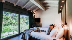 A bedroom with a large window, a bed with pillows and a tray, a bedside table with a candle, and a TV on a stand. - Villa Violetta (Menaggio)