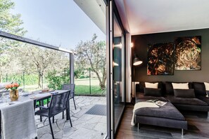 Een moderne woonkamer met een bank, een eethoek met een tafel en stoelen, en een grote glazen deur die uitkomt op een tuin.