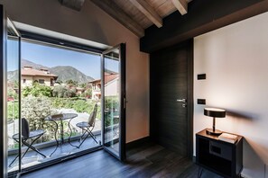 Een moderne kamer met een schuifdeur naar een balkon, een kleine tafel met stoelen en een nachtkastje met lamp.